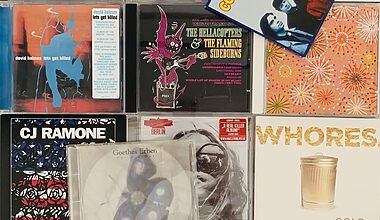 Photograph of a random lot of 13 CDs that were decluttered. The CDs are laid out in a tiled fashion and we can see some artists like CJ Ramone, The Hellacopters and Collective Soul for example.