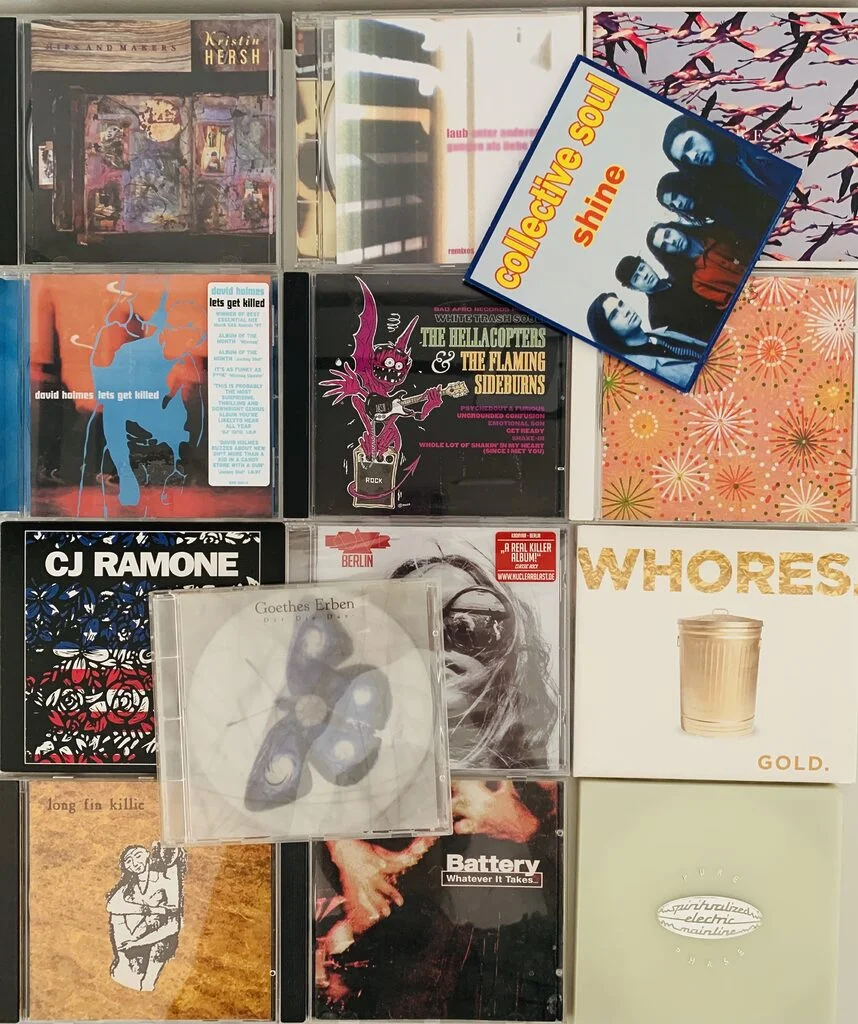 Photograph of a random lot of 13 CDs that were decluttered. The CDs are laid out in a tiled fashion and we can see some artists like CJ Ramone, The Hellacopters and Collective Soul for example.