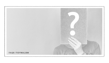 Low-contrast grey and white photo for an FAQ page of a woman holding a big question mark on a piece of paper in front of her face.