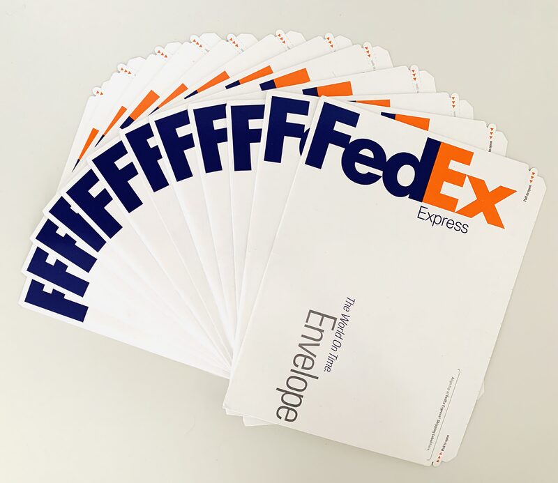 Photograph of 12 FedEx mailing envelopes spread out in a fan on a white table.