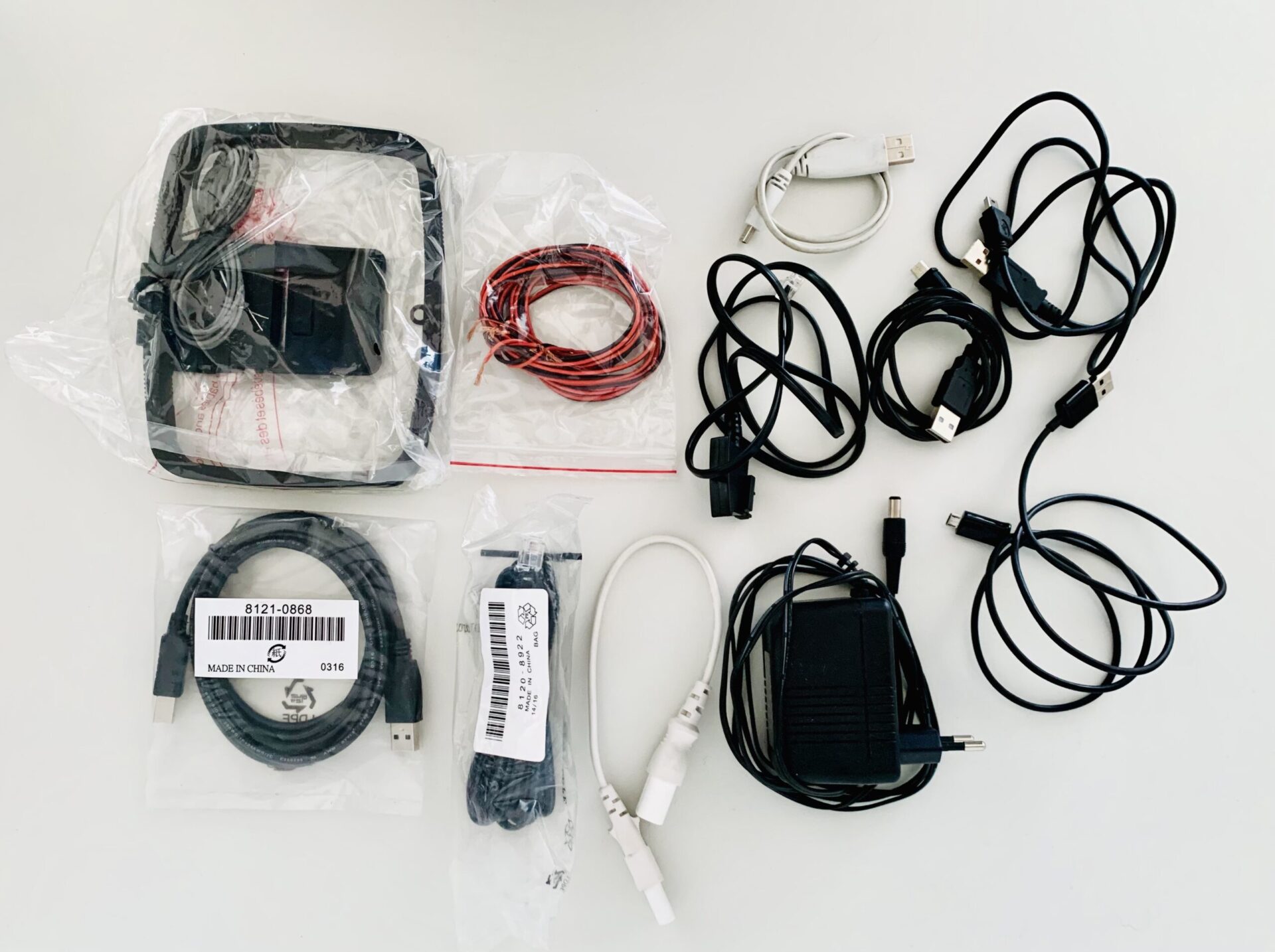 Photograph of e-waste or tech waste, laid out on a white table and photographed from above. Items include power plugs, an analog antenna, and random cables.