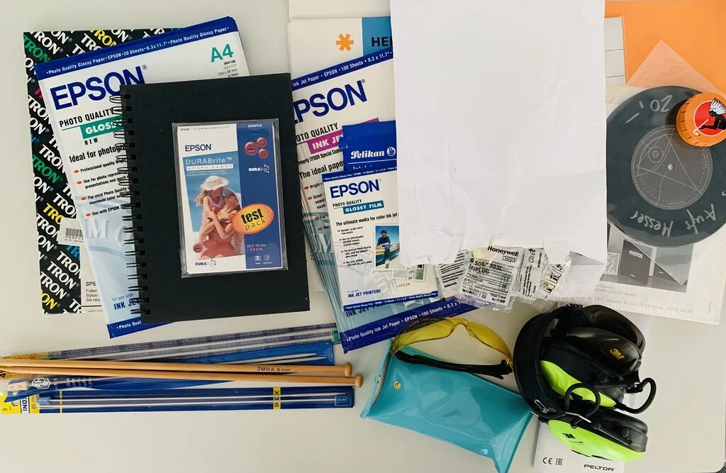 Photo of a bunch of hobby items that were decluttered during a 30 day minimalist game. the hobby supplies include packets of photo inkjet paper, notebooks, knitting needles of different sizes, a 7 inch single, and ear protection usually worn at shooting ranges.