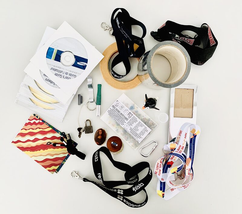 Photo of around 25 pieces of random items typically found in a junk drawer such as masking tape, keychains and lanyards, old CD-Roms, a luggage lock and key, and a hook.