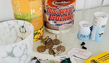 Photo of items from a kitchen clearout decluttering session, including magnets, protein powder, water filters, takeaway menus, and a bottle opener. All the objects are set on a white table in front of a white wall.