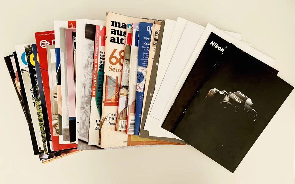 Photo of a stack of old magazines and product brochures laid out on a white table in a fan shape.