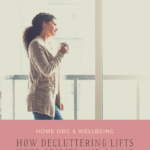 Woman standing at her balcony window looking outside. She has her head leaned on the glass door and is smiling. The room is very tidy and uncluttered. In her right hand she's holding a cup of coffee. Caption reads: Home Organization and Wellbeing: How Decluttering Lifts Your Spirits and Calms the Mind. tidymalism.com.