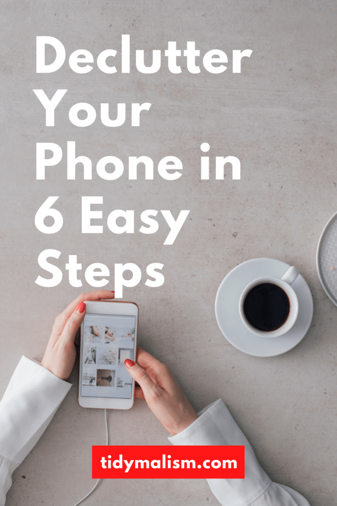 Image of two lady's hands from above, holding a white smartphone. To the right is a coffee in a white porcelain cup. The smartphone, lady's sleeves and tabletop are all white. Caption reads Declutter Your Phone in 6 Easy Steps, tidymalism.com.