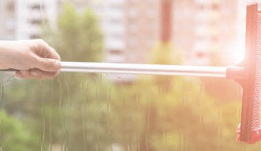 Window washing before the hot weather starts is just one thing you should have on your to-do checklist to get organised for summer. Image shows a hand pulling a squeegee across a freshly washed window. The weather looks warm and summery. The image is for a blog post about getting everything at home organised for the summer so that you can enjoy the warmer weather without worrying about chores, housekeeping, or home repairs and maintenance.