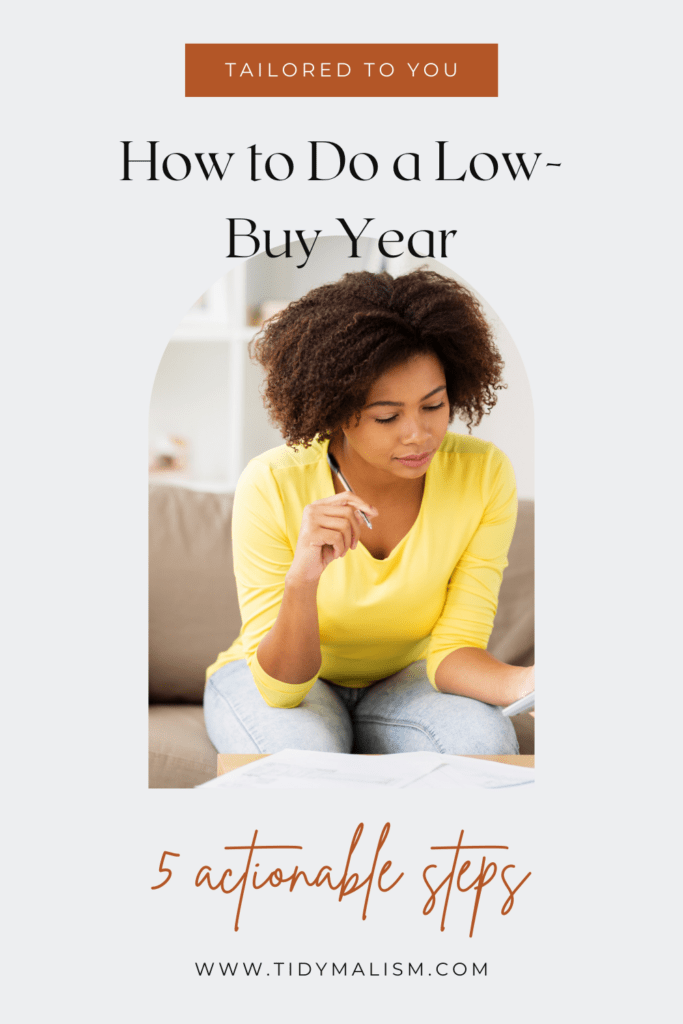 Young lady in a yellow shirt, sitting on the couch, holding a pen in her hand and looking over her accounts. Caption reads: Tailored to you: how to do a low buy year. 5 actionable steps. www.tidymalism.com