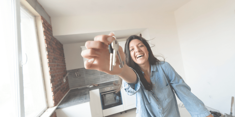 Excited young lady holding up the keys to her new apartment and smiling with joy.