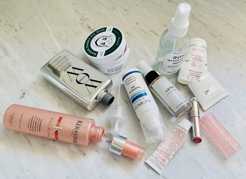 Close up photograph of an assortment of empty beauty products. Tubes, plastic vials, glass bottles all randomly lying about on a marble countertop. Some of the bottles are open and lying on their side. Some of the tubes are cut in half and we can see that the remainig product was really used up.