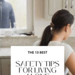 Young lady sitting at her countertop on her laptop. At the window beyond her left shoulder, we can see an intruder spying on her. He is wearing black and a black ski mask. Caption reads The 13 Best Safety Tips for Living Alone.