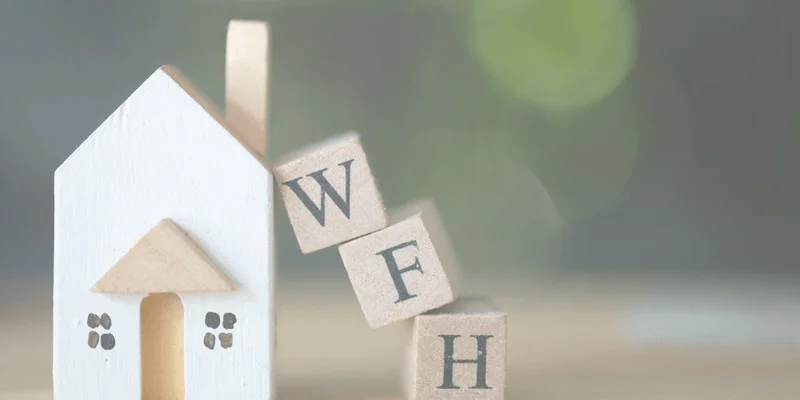 Miniature wood house with miniature cube-shaped letters spelling out "WFH" for work from home.