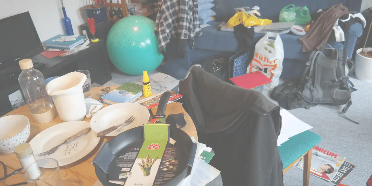 Messy, cluttered and dirty room, with items strewn everywhere and dirty dishes on the dining table.
