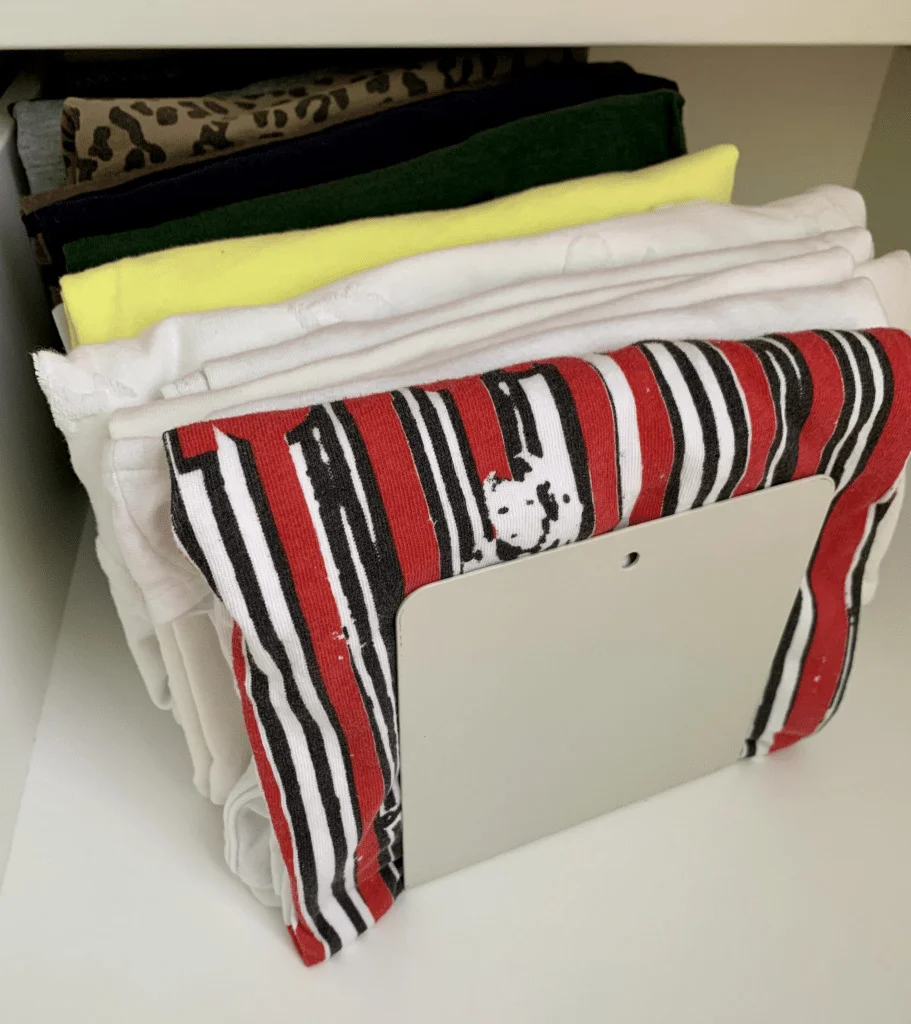 File folded t-shirts being held up by a bookstand.