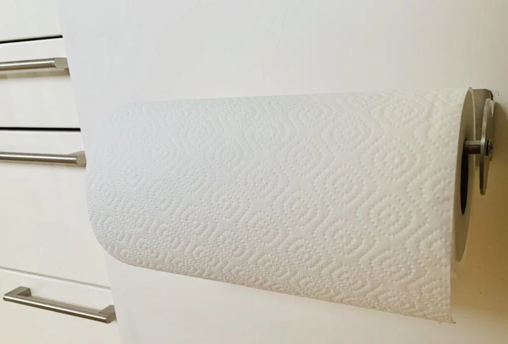 Photo of a stainless steel paper towel holder with a roll of white paper towels on it, hidden inside of a lower cabinet in a small kitchen to maximise space.