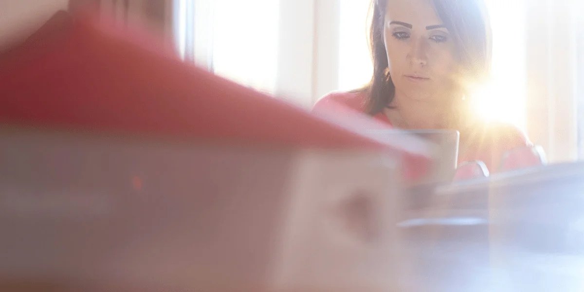woman sitting a her table with bright sunlight streaming in the window behind her.