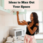 Long-haired black woman in her late twenties or early thirties, dressed in a belted pastel pink printed skirt and black top, organizing her kitchen cabinets. Her dishware is white and the cabinets are a pastel mint color. There is a white microwave in the corner and her small kitchen is spotless. Caption reads 10 small kitchen ideas to max out your space.