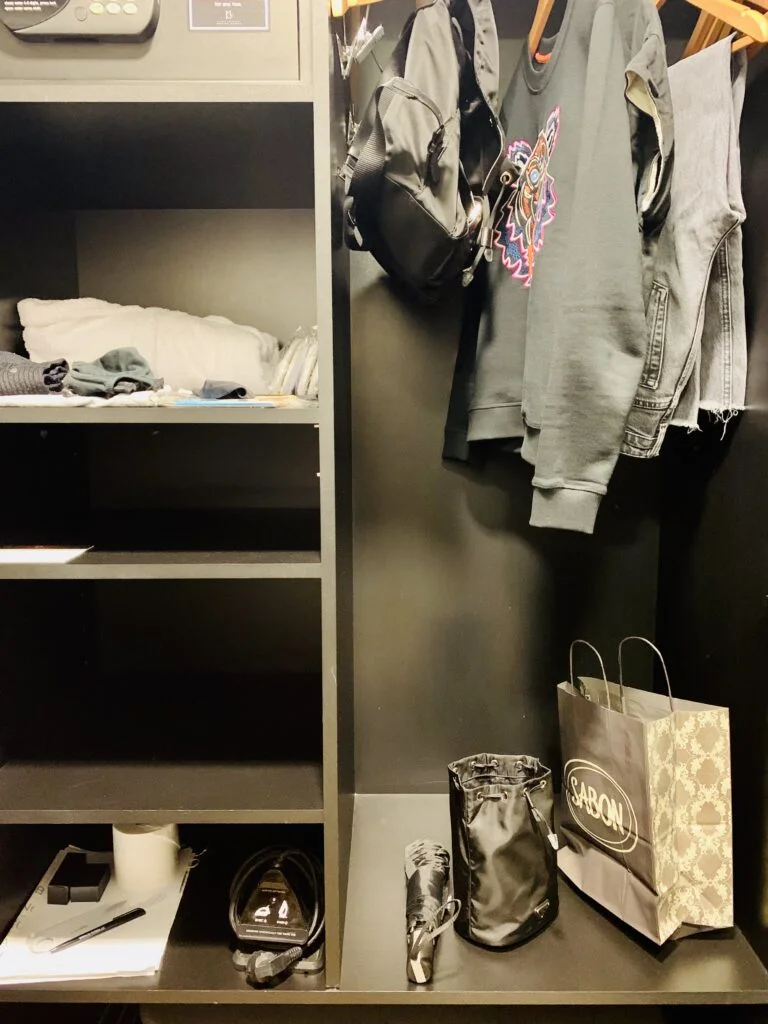 Photograph of a hotel room closet showing how to stay organised in a hotel room. The guest has kept her things tidy and sorted, and is using a repurposed shopping bag for her dirty laundry, which she keeps at the bottom of the closet so she can easily toss in her dirty laundry at the end of the day.