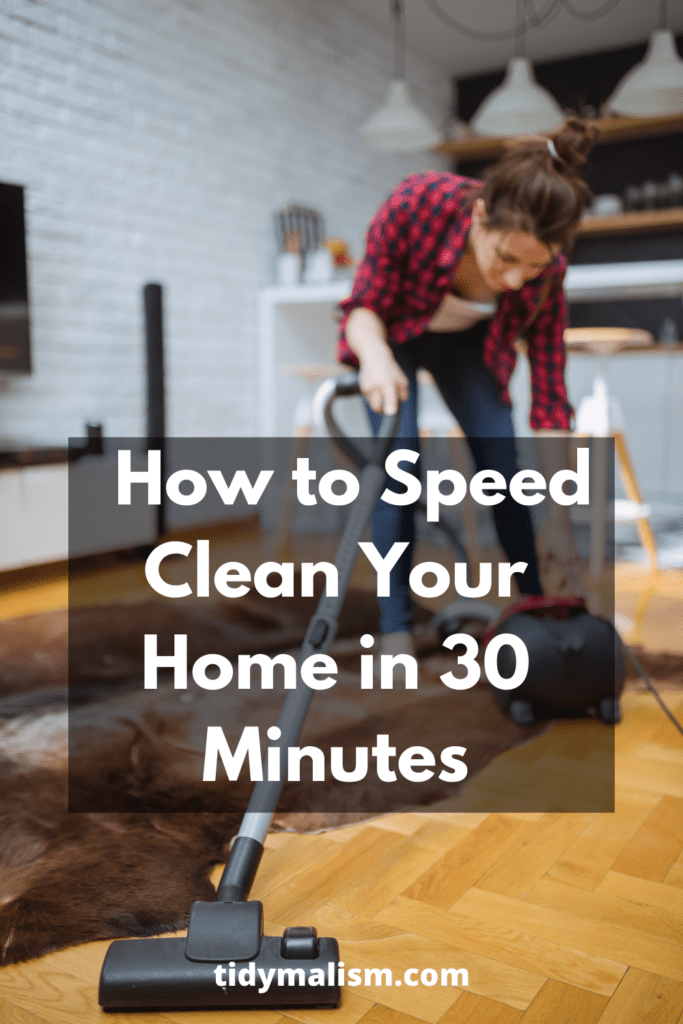 Young lady in red flannel shirt quickly vacuuming her living room hardwood floors and area carpet. She is hunched over her hoover to pull its cable out. Caption reads how to speed clean your home in 30 minutes.