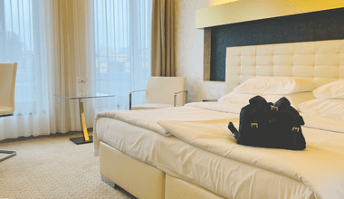 Photograph of a very organized hotel room. The bed is made and there is a small Prada backpack on the bed.