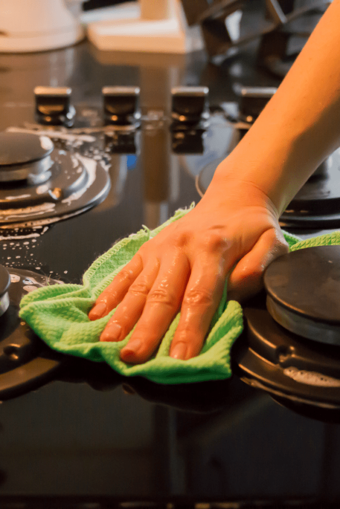 A white hand wiping down the kitchen hob with a light green cloth.