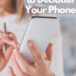 Cropped photo of a blond lady holding a white, XL smartphone in her French-manicured hands. She's wearing a white long-sleeved top and a steel watch, holding the phone in her left hand, and tapping into it with her right hand, which is also holding a pen. Caption reads 6 easy steps to declutter your phone.