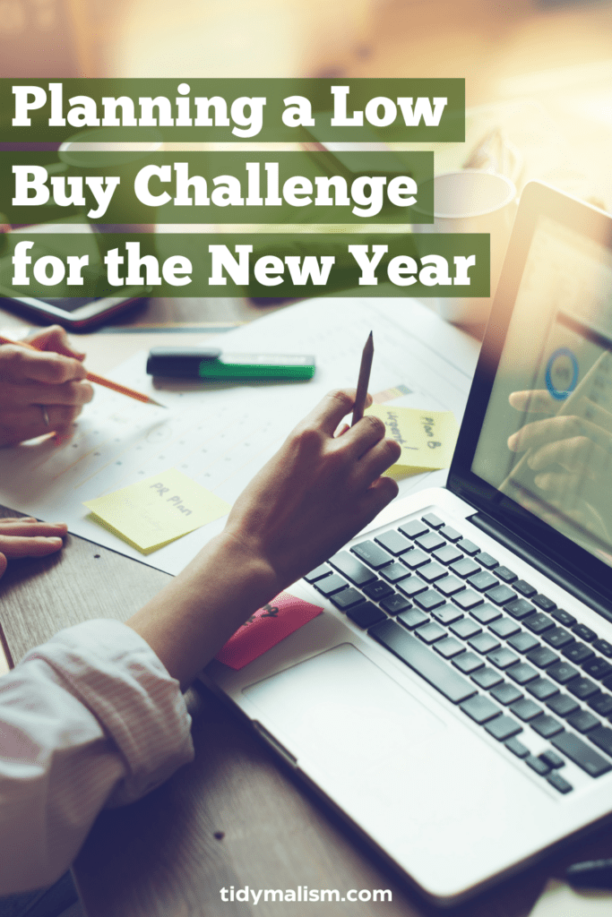 Cropped photograph of two different people's white hands, each holding pens and pencils. They are sitting in front of an open laptop. Spread out on the desk are papers and post-it notes. They seem to be planning something. Caption reads Planning a Low Buy Challenge for the New Year.