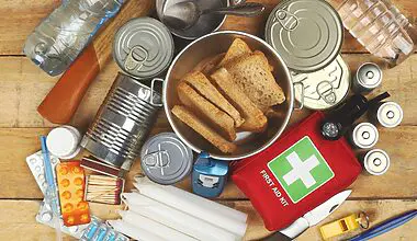 Cropped photograph of assorted emergency supply items such as water, batteries, a first aid kit, candles, bread and matches.