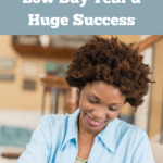 Photo of a thirty-something black woman in a blue blouse sitting at her desk and balancing her checkbook. She's smiling. Caption reads: How to make your low buy year a huge success.