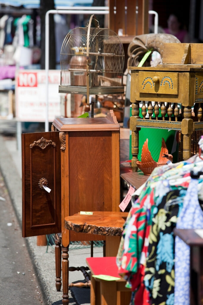 Photograph from a flea market showing old furniture, mostly made out of wood, an old birdcage, various textiles.