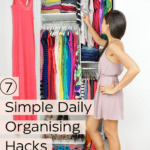 Lady standing to the right of her small closet, looking inside. Her clothes are very tidily stored, there is no clutter and her garments are organized by color in the closet. Caption reads: 7 simple daily organising hacks.