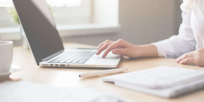 Cropped photo of a white woman's hands at her laptop, going through a digital spring cleaning checklist.