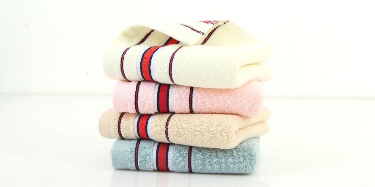 Stack of towels in pastel colors from the same style range, with a red and navy stripe at the ends.