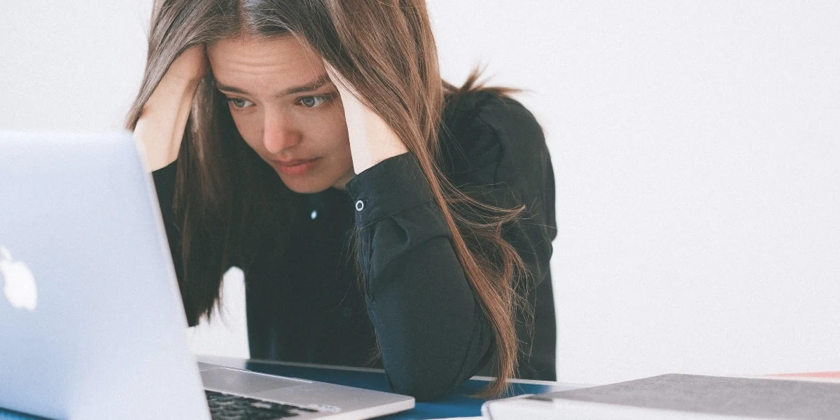 What is mental clutter? Photo of a young woman with long brown hair hunched over her laptop, cradling her head in her hands and looking very worried.