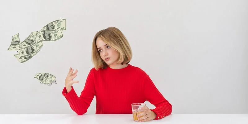 Young blond woman sitting at an empty white table. Dollar bills floating out of her hands. All that clutter used to be money.
