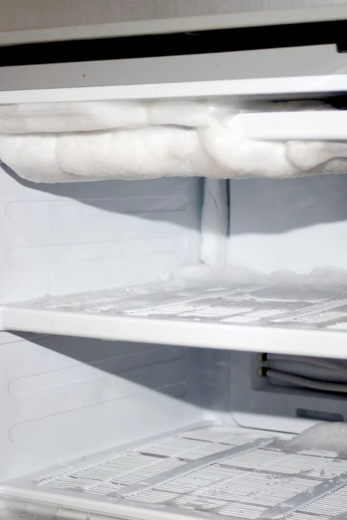 Cropped photo of a freezer in need of defrosting, with thick chunks of ice on its ceiling and floor.
