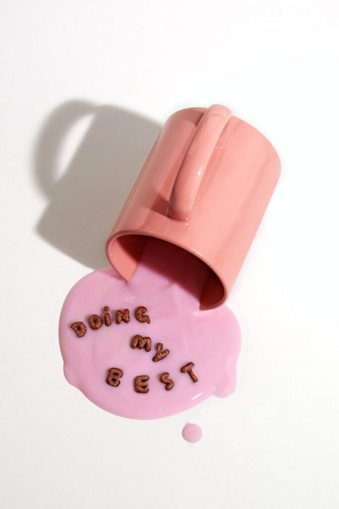 A pink mug lying on its side with a faux pink liquid spilling out of it. Letters in the liquid spell out "doing my best."