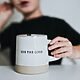 Cropped photo by Nathan Dumlao of a young person sitting at a table, with hand on a mug that has a positivity message "see the good."