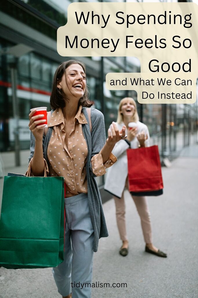 Two women in their late twenties on a shopping street with bright red and green shopping bags over their arms, and Starbucks coffees in their hands. They appear to be laughing and having a great time, illustrating an article titled why does spending money feel so good.