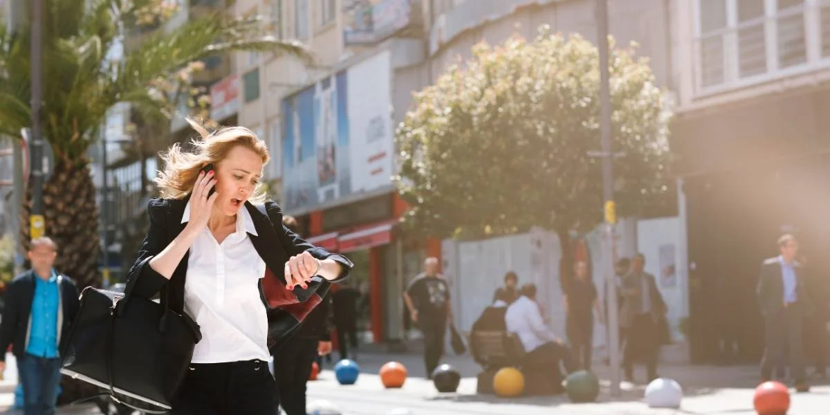 Woman dressed in business apparel running down the street while telephoning and looking at her watch.