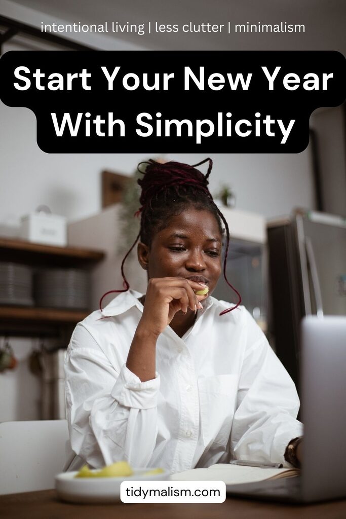 Young black woman with hair pinned up, wearing a white blouse and reading at her desk while eating a snack from a plate set to her right. Photo is for an article about building simplicity habits in the new year.
