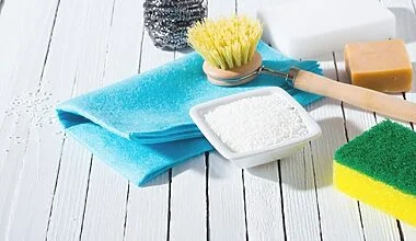 An assortment of simple cleaning materials for the bathroom including baking soda, natural bristle scrub brush, soft cloth and scrubbing sponge.