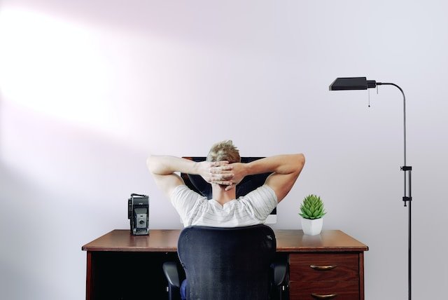 Photograph by Jason Strull of the back of a man at his desk, with his arms stretched behind his head.