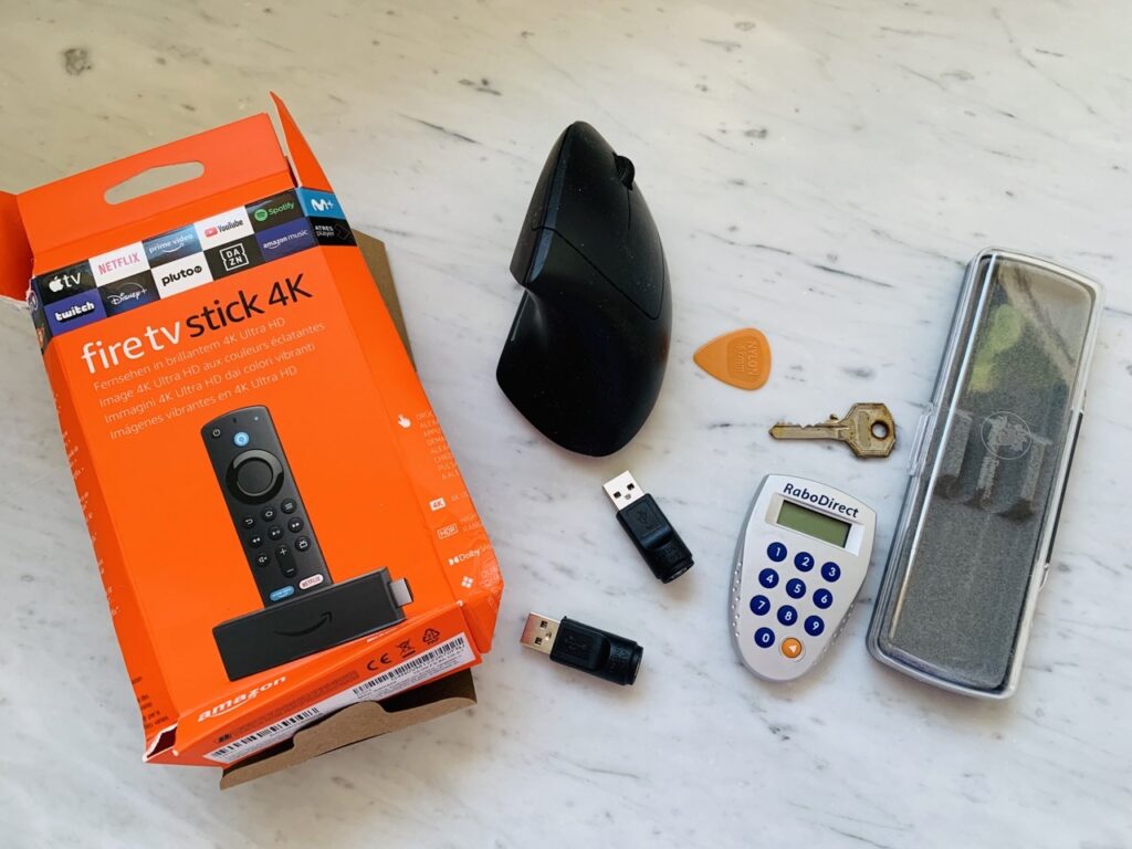 A motley assortment of junk decluttered during a minsgame challenge, including adapters, a guitar pick, an old ergonomic mouse, and the empty packaging from an Amazon Fire TV stick.